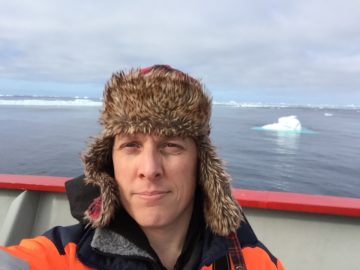 A man on a boat with icebergs and the sea in the background