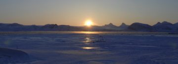 A sunset over a body of water with a mountain in the background.