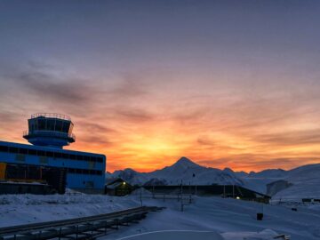 A sunset over the snow with a blue building on the left