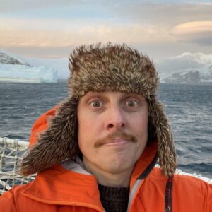 A man in orange shirt sitting in front of a body of water