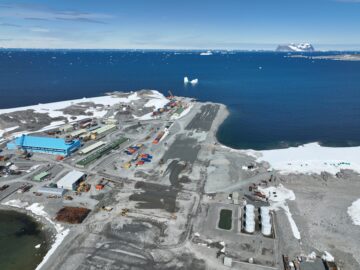 Aerial view of runway and large blue building and blue sea in background