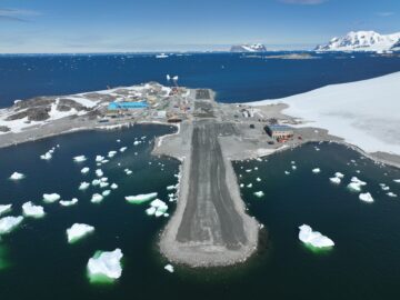 view of a runway from the air with icy waters and snowy mountain surrounding the runway.
