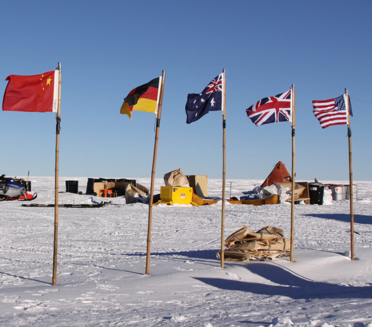 A twin otter at a field camp with flags of China, Germany, Australia, the UK and United States in the foreground