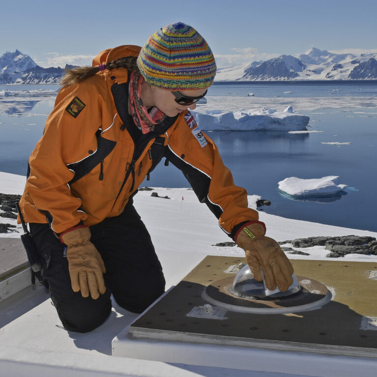 A scientist maintaining an optical instrument on an ice shelf.