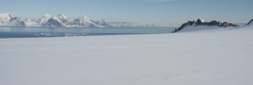 A snowy landscape with the sea in the background
