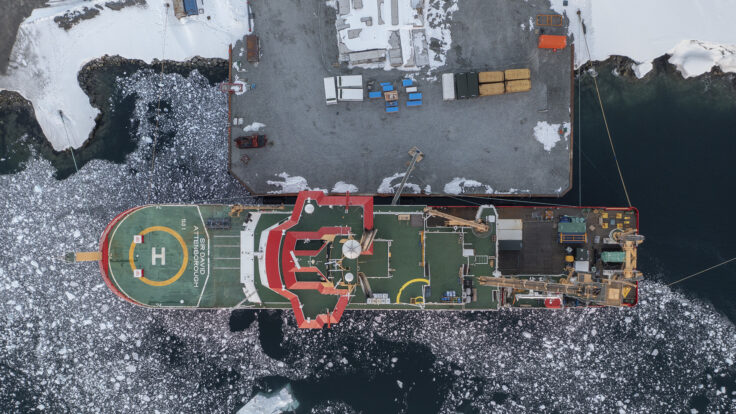 Aerial image of RRS Sir David Attenborough docked at Rothera Research Station wharf surrounded by floating ice
