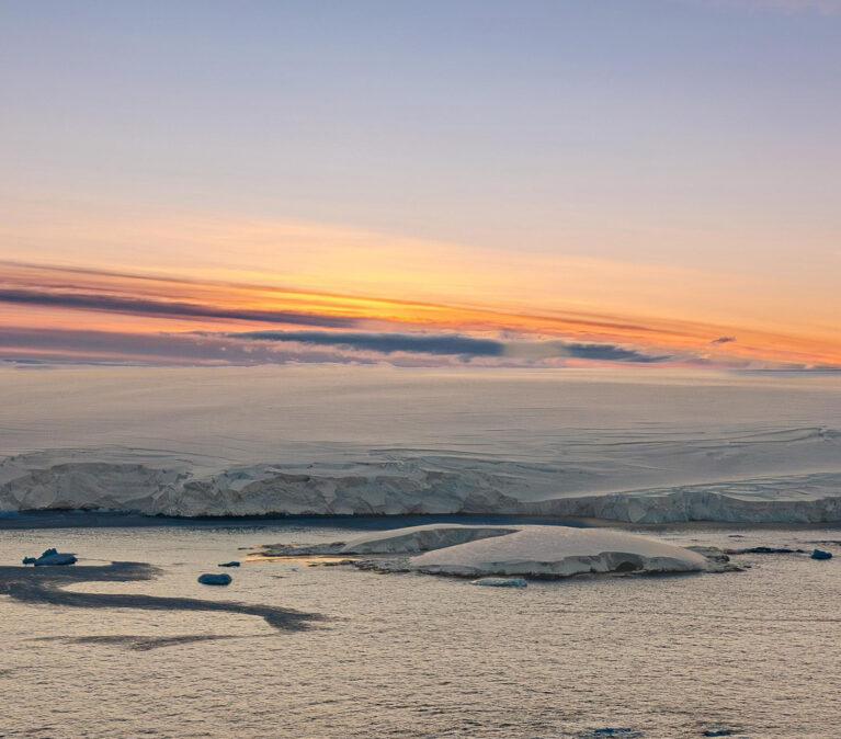 An Antarctic sunset. The ice shelf meets the sea with mountains in the background