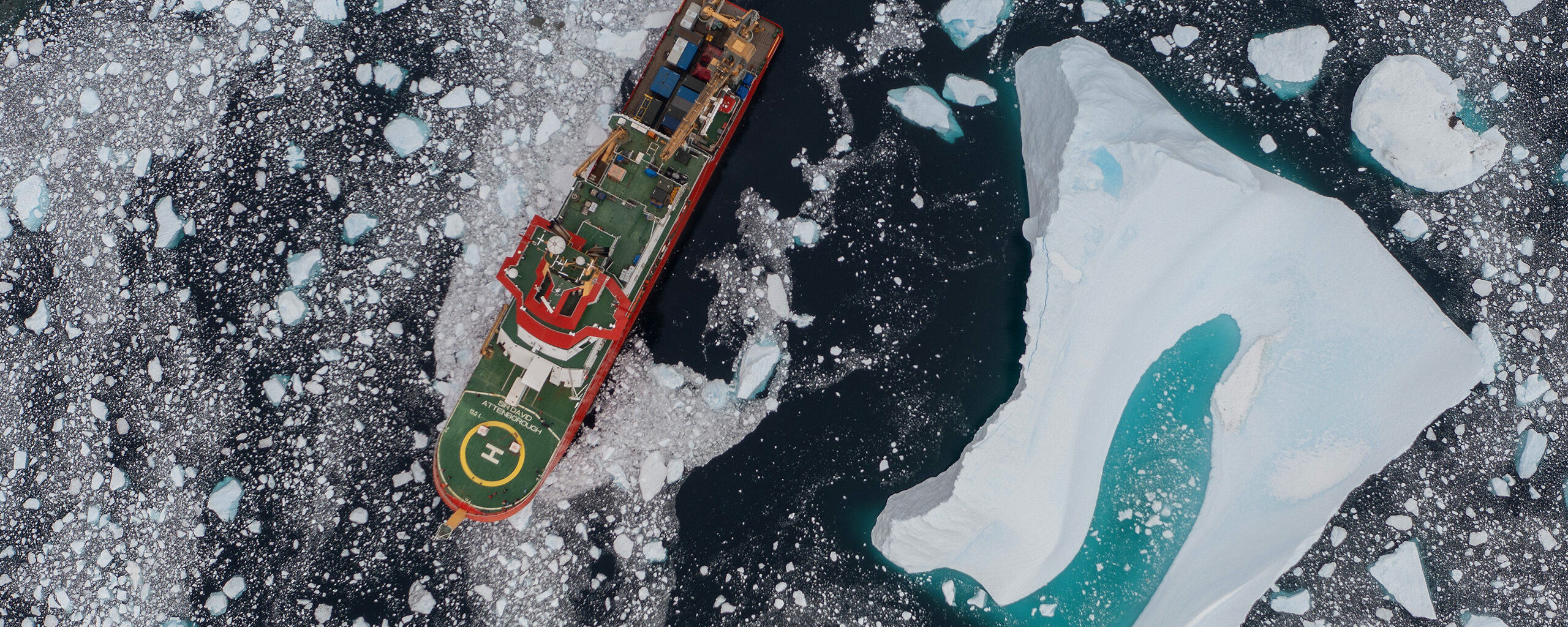 An aerial image of RRS Sir David Attenborough sailing near an iceberg