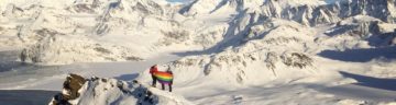 People on a snowy mountain range holding a rainbow flag