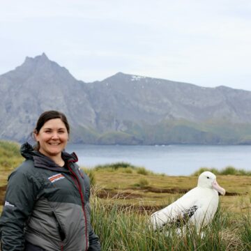 A man standing in front of a lake with a mountain in the background