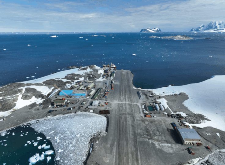 An aerial photograph showing the Rothera Research Station bisected by its runway. In the distance icebergs can be seen floating in the ocean